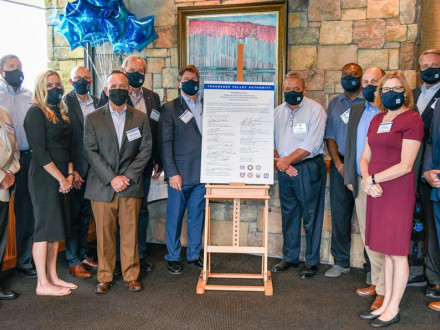 Los representantes tanto de TVA como de los sindicatos promueven su asociación con una extensión del contrato de diez años. A la izquierda del cartel, primera fila de izq. a der., Megan Flynn y Mike Skaggs. Fila trasera de izq. a der.: David Tolley, UA; Brandon Bishop, administrador del Consejo por Hora; Curtis Sharpe, IBEW; David Beckler, administrador del Consejo Anual y Jeff Lyash, TVA. A la derecha del cartel, primera fila, Sue Collins, TVA. Fila trasera de izq. a der., el representante internacional Du