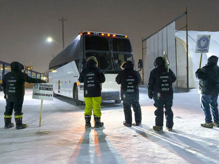 A pesar de las temperaturas de -20F/-29C, los Boilermakers excluidos del L-146 se mantienen firmes en la línea de piquete mientras se acerca un autobús lleno de trabajadores sustitutos.  La sede sindical Internacional ha proporcionado abrigos y pantalones de nieve para mantener a los Boilermakers calientes en la línea de piquete.