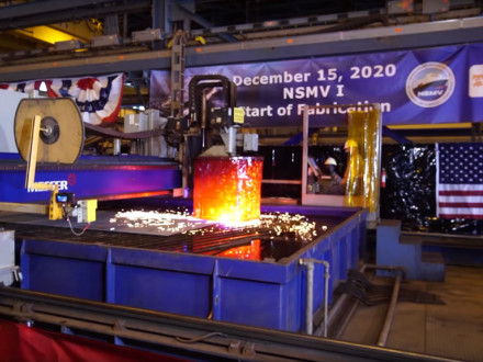 A plasma cutting machine makes the first cut in a steel plate.  The pieces will be transported to an assembly line where they will eventually become part of the ship's keel.