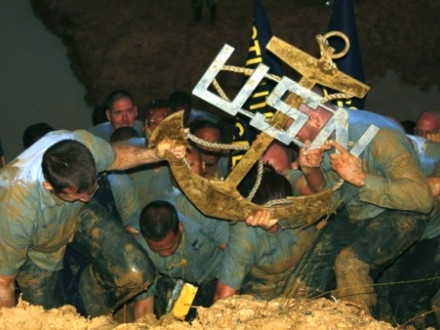 Wet, cold, and hungry, newly-minted Navy CPOs charge up a muddy hill carrying a symbolic anchor made by Local 154 members.